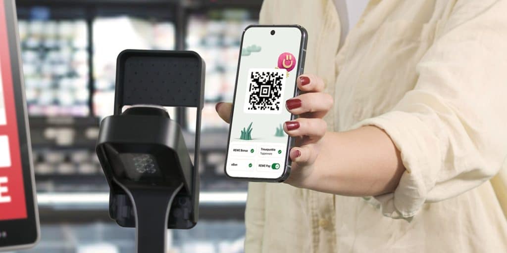 Eine Person hält ihr Handy mit geöffneter REWE App vor einen Scanner an der Kasse, um REWE Pay und das Bonusprogramm zu nutzen.
