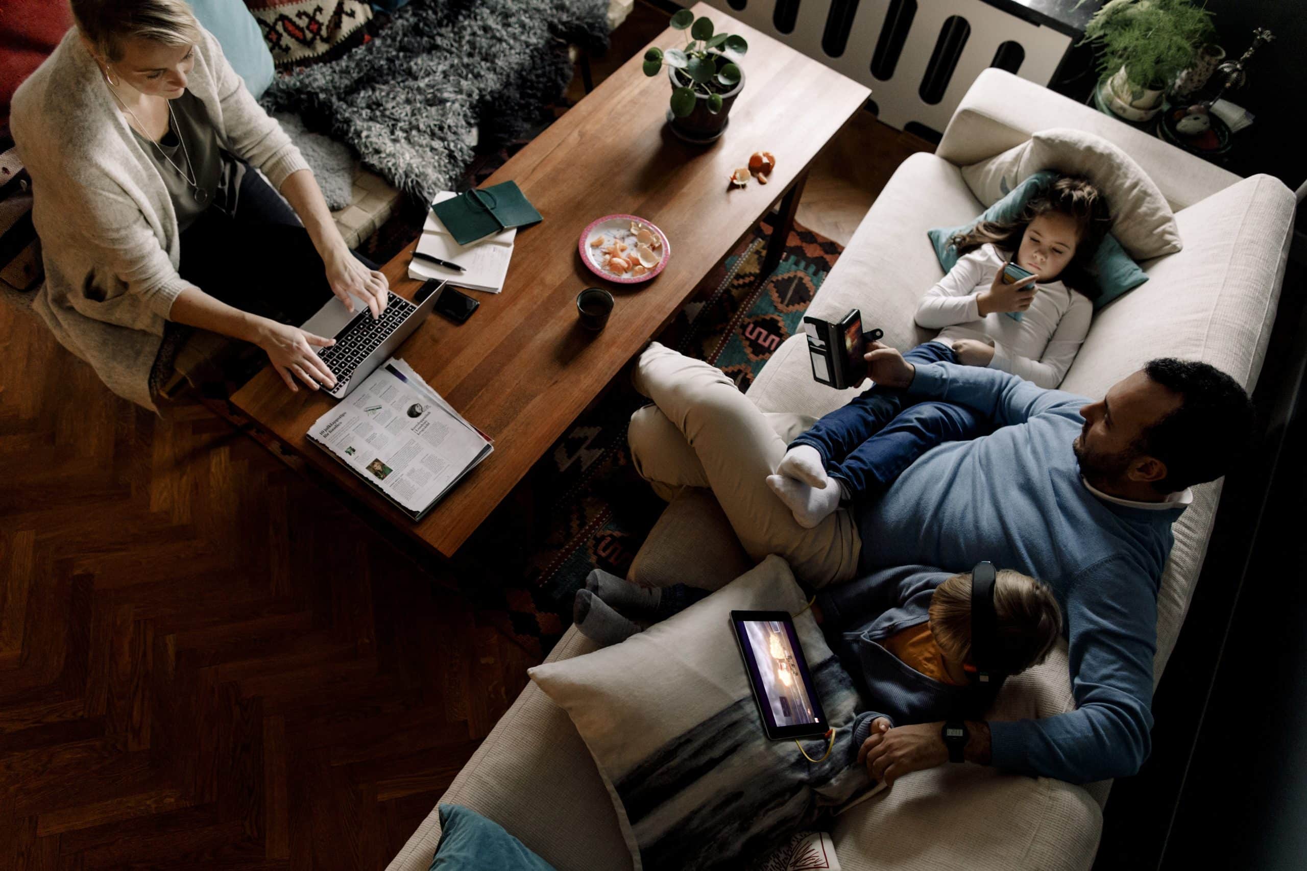 Familie nutzt gemeinsam verschiedene digitale Geräte im Wohnzimmer.
