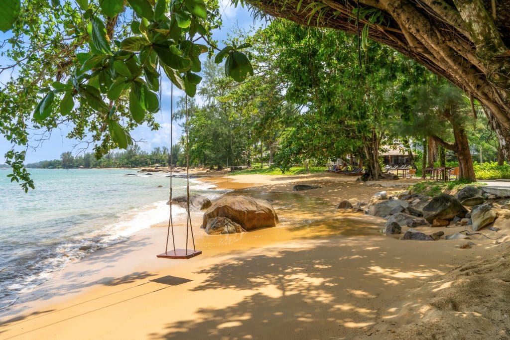 Strandabschnitt mit grünen Bäumen und einer daran befestigten Schaukel in Thailand.