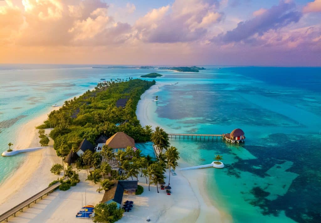 Luftaufnahme von einem Hotelkomplex auf einer kleinen Insel der Malediven, umgeben von blauem Wasser.