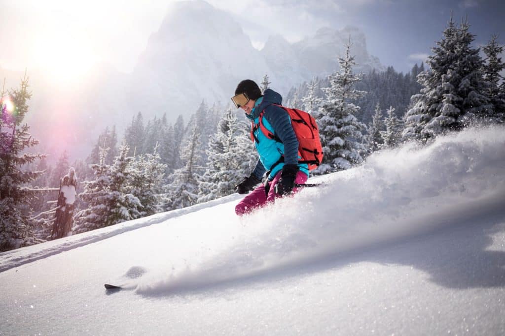 Eine Person fährt bei Sonnenschein auf einem schneebedeckten Berg Ski.