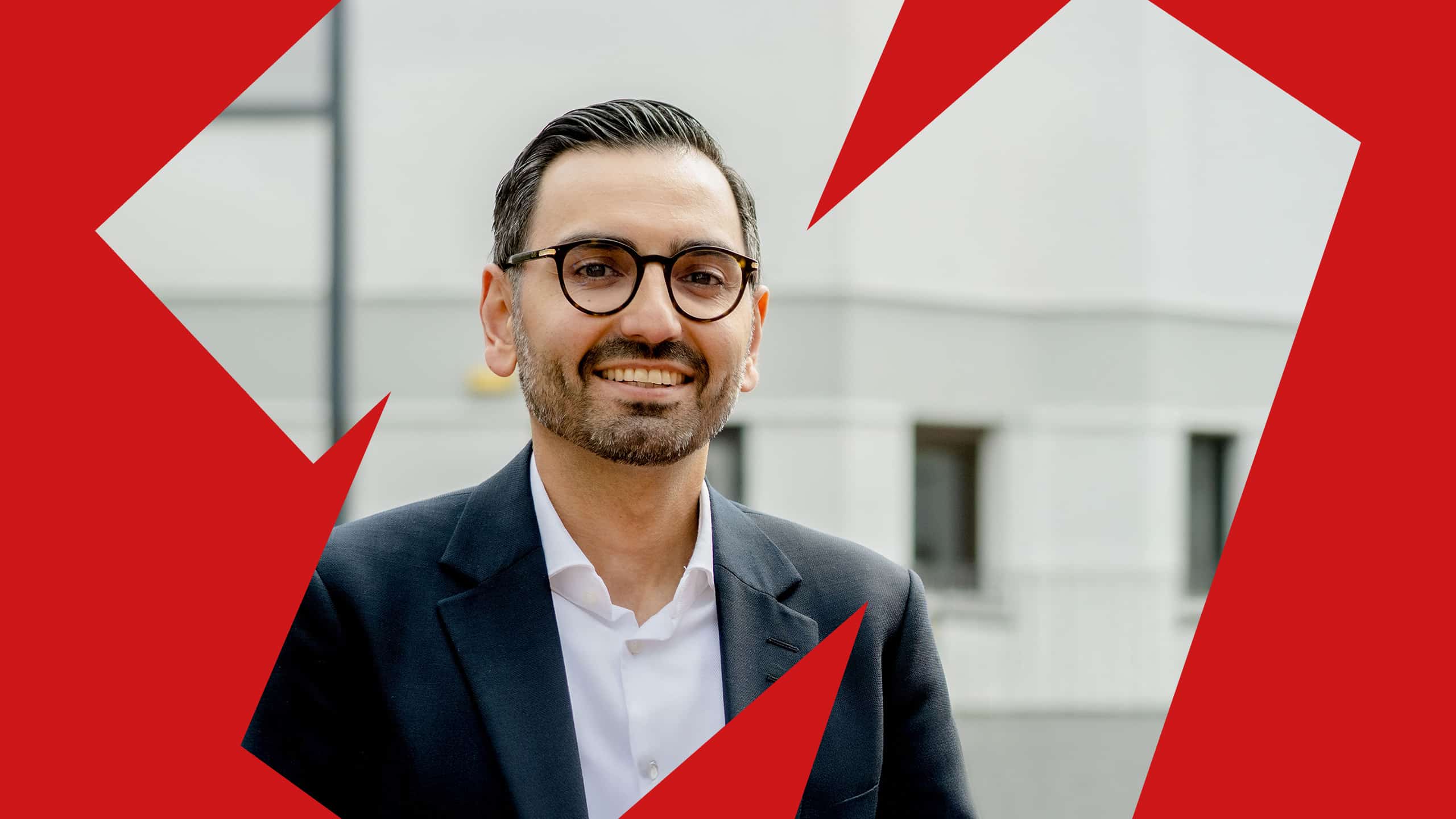 Porträt von Karim Fereidooni. Er lächelt in die Kamera. Ein rotes grafisches Element umrahmt das Porträt.