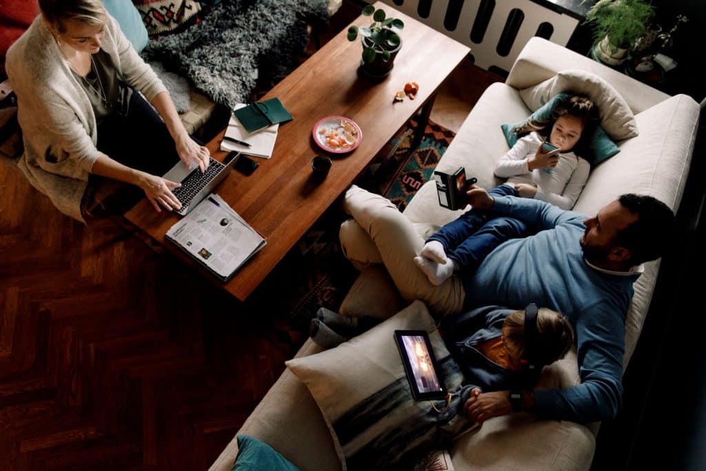 Eltern und Kinder mit Laptop, Smartphone und Tablet auf dem Sofa.