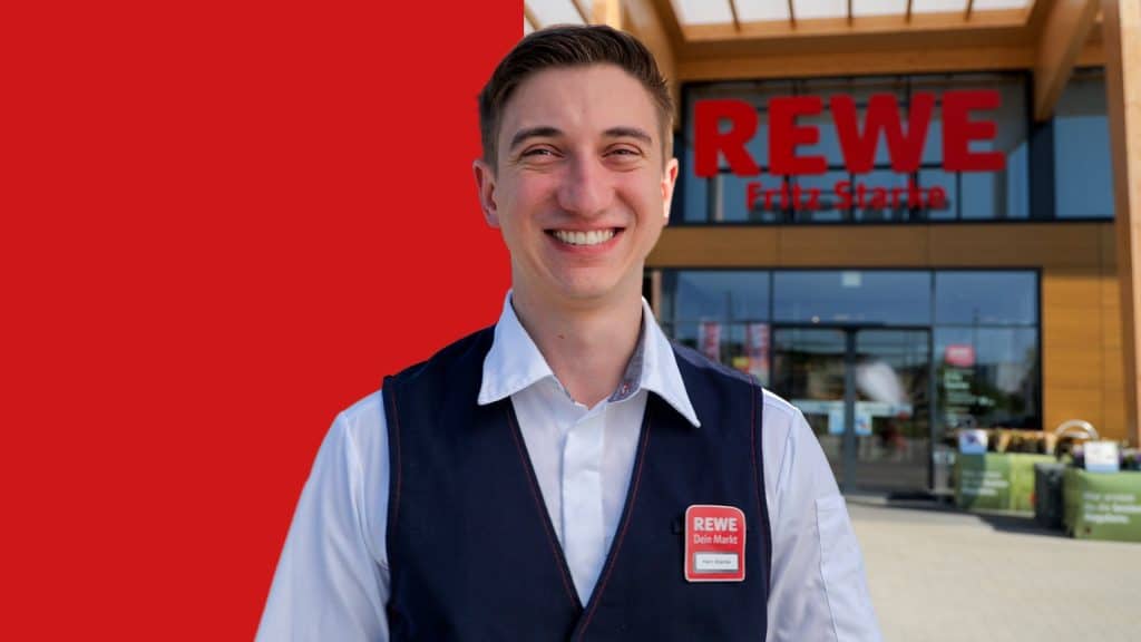 Porträt von Fritz Starke vor seinem REWE Markt. Der Hintergrund ist zur Hälfte mit einem roten Balken hinterlegt.