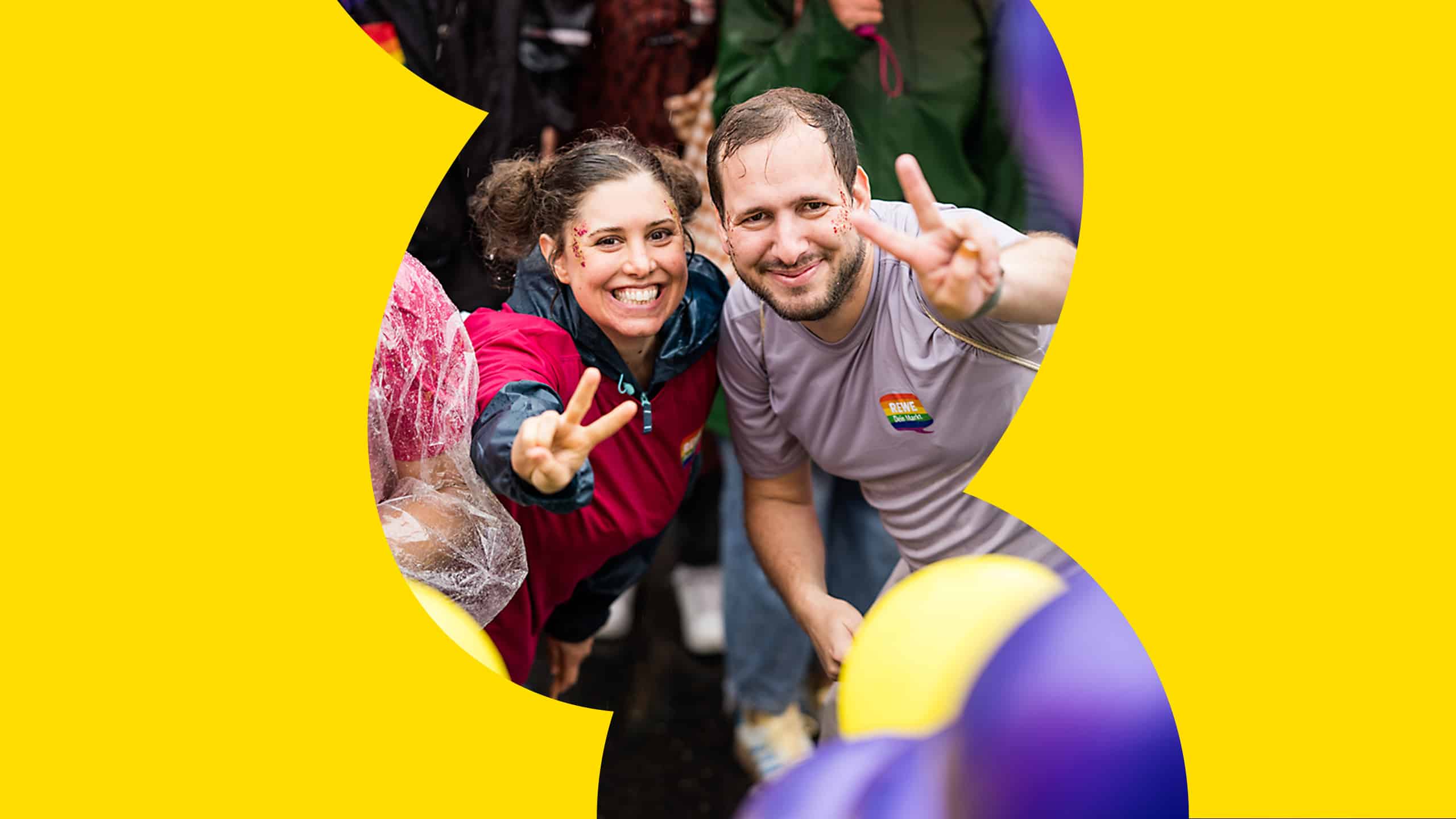 Zwei Personen mit buntem Glitzer im Gesicht lachen in die Kamera und sind umgeben von bunten Luftballons.