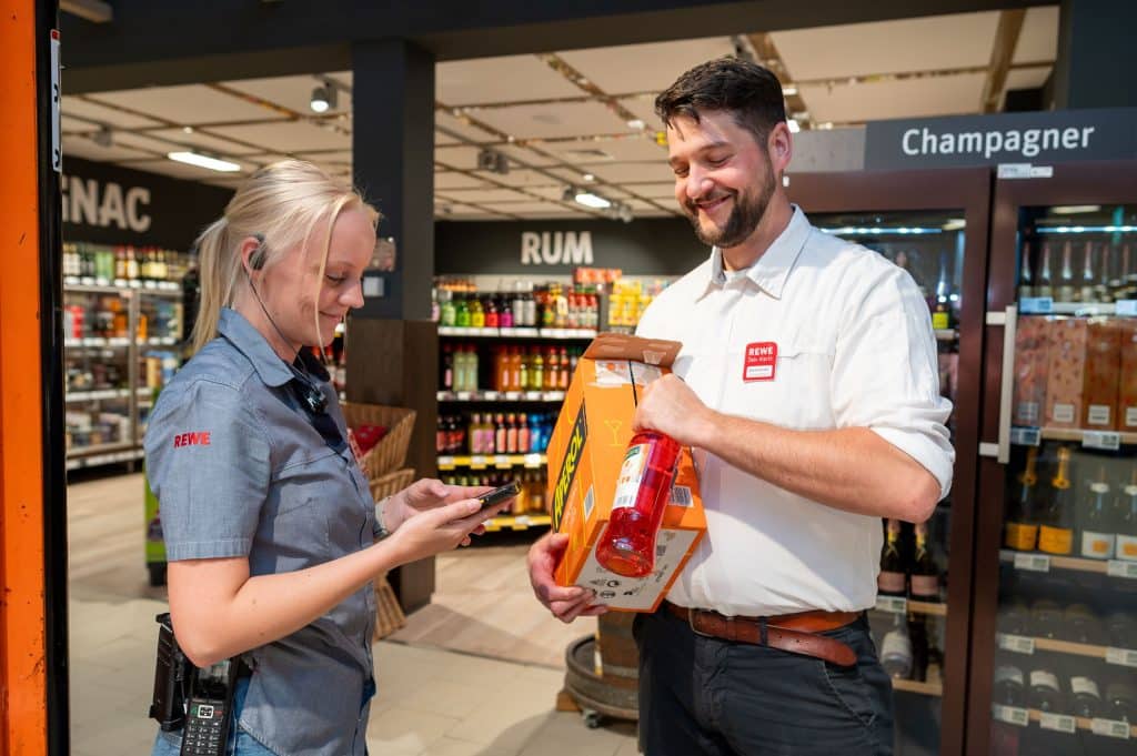 Zwei Mitarbeitende in einem Supermarkt stehen im Spirituosenbereich und sprechen miteinander