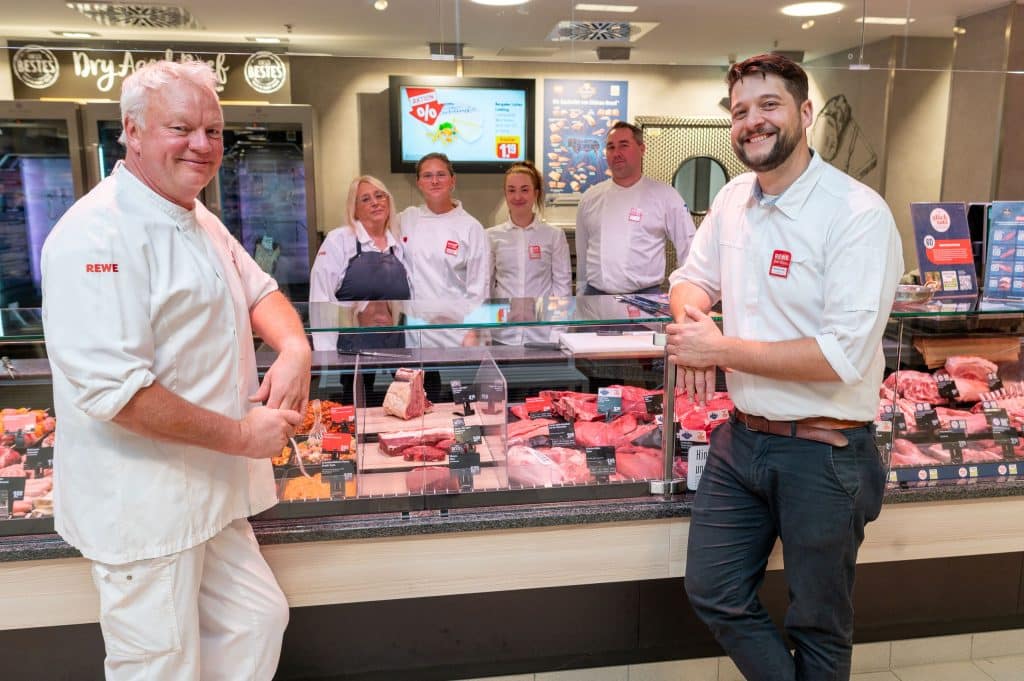 Mehrere Mitarbeitende stehen hinter einer Fleischtheke in einem Supermarkt.