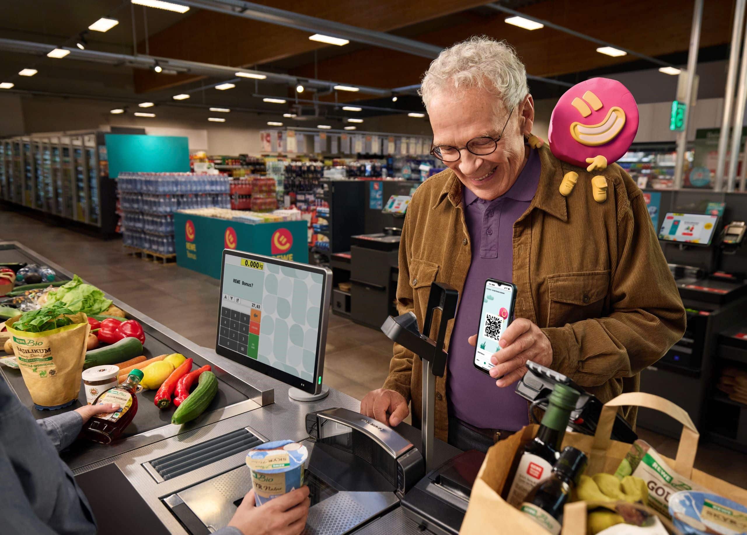 Älterer Mann an REWE Kasse mit REWE Bonus auf dem Handy