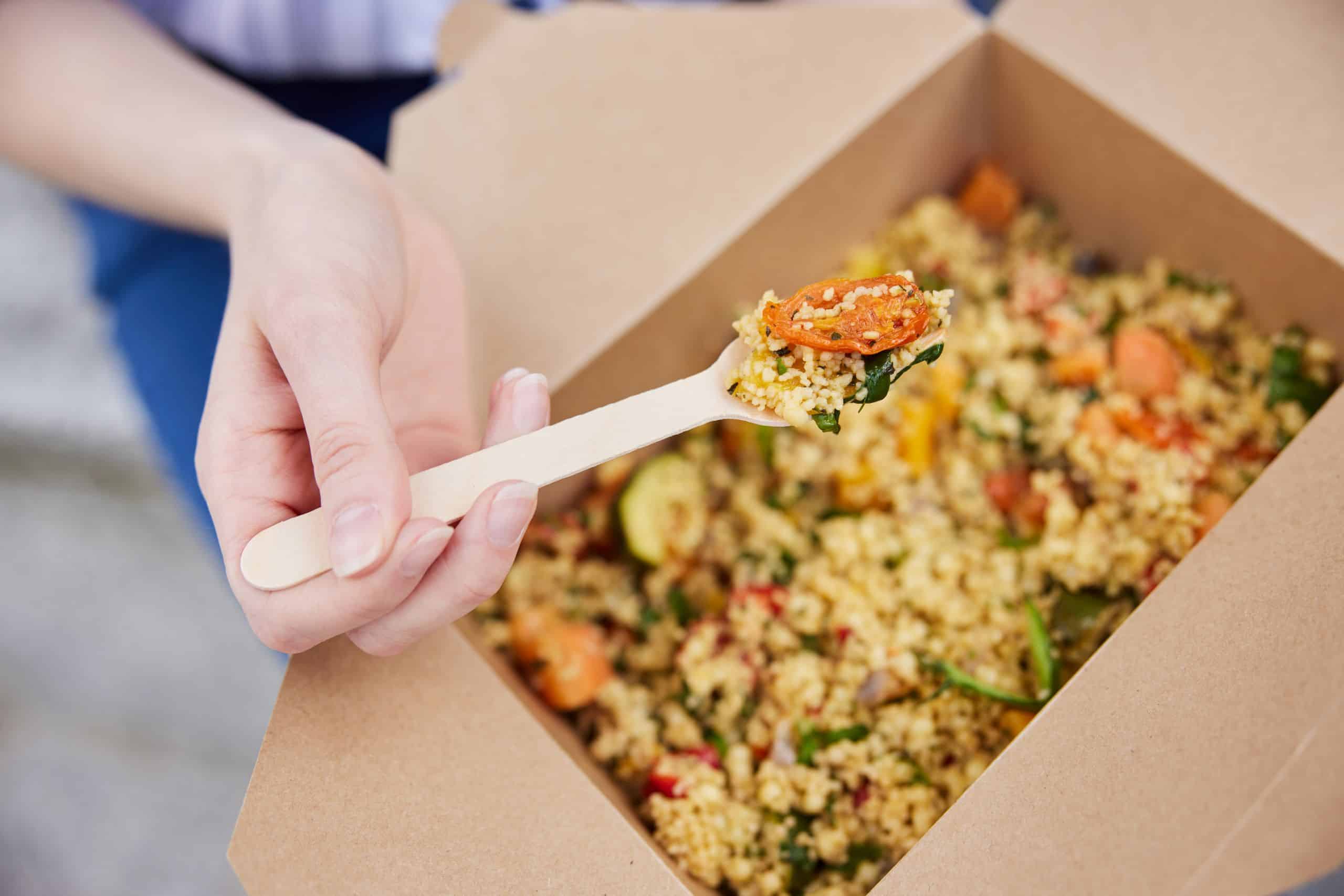 Nahaufnahme der Frau Essen gesunde Vegan oder vegetarische Zumende Mittagessen aus recycelbaren Verpackung mit Holzgabel.
