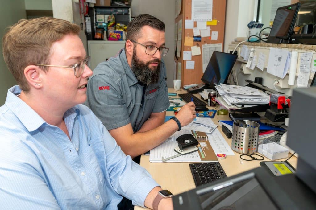 Sebastian Stein und seine Frau sitzen an einem Tisch im Büro und schauen auf einen Computerbildschirm.