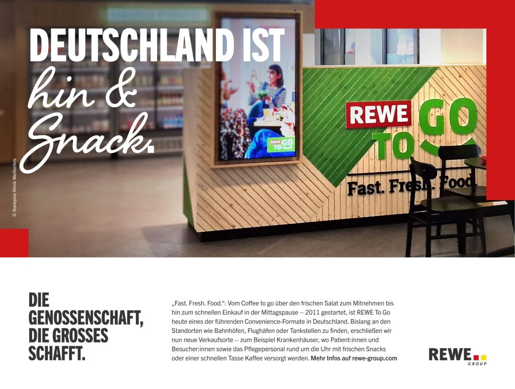 Innenaufnahme eines REWE To Go Bereichs mit Sitzplatz vorne, Holz- und Grün-Design, großem Text: 