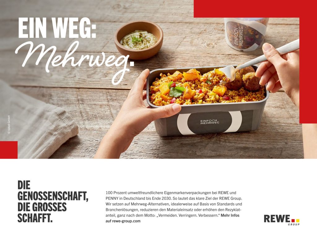 Nahaufnahme eines Mehrweg-Essbehälters mit einem bunten Gericht auf einem Holztisch, während Hände mit Besteck essen und der Text: 