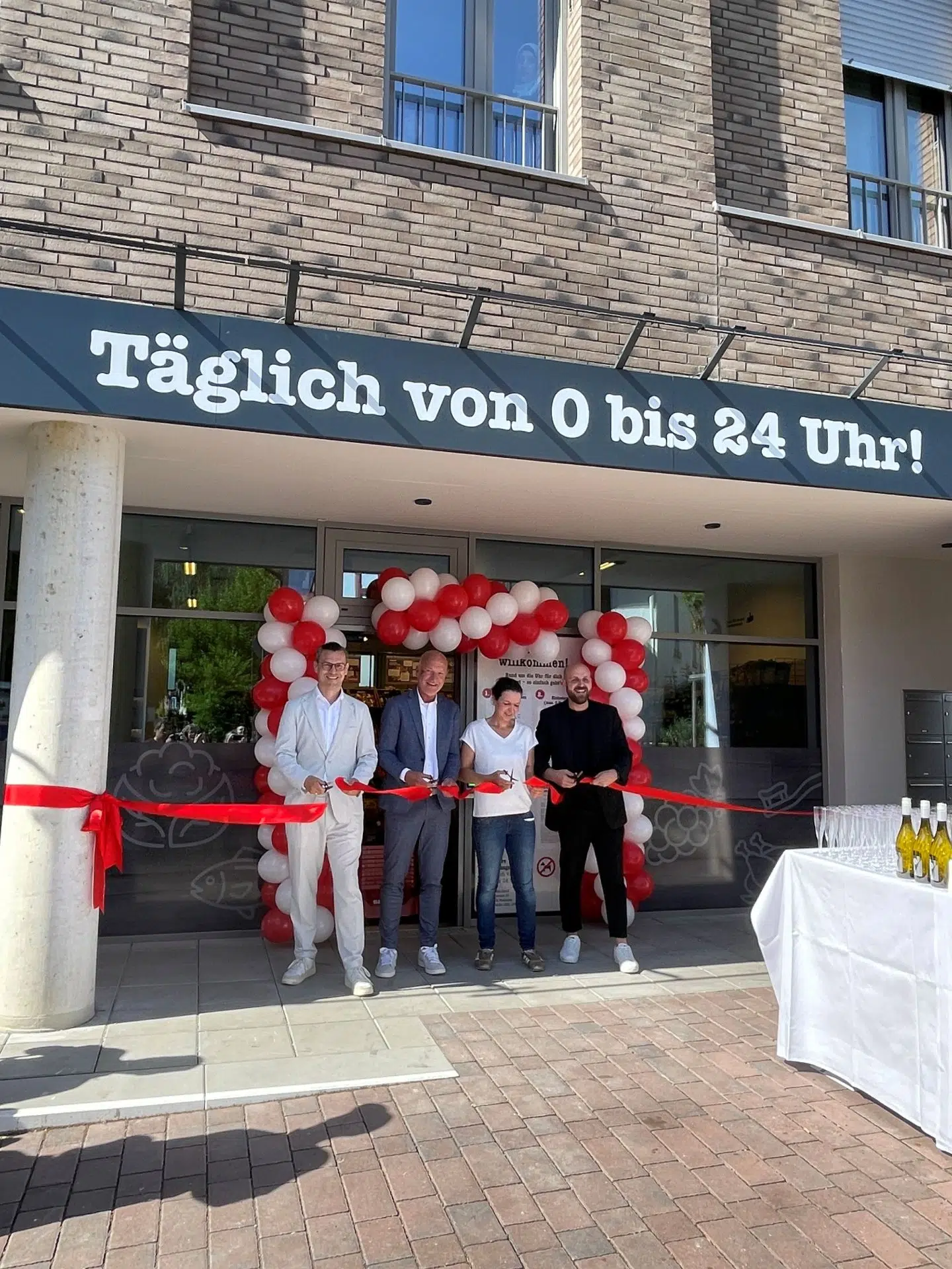 Vier Personen eröffnen einen „Paolos nahkauf Box“ feierlich mit einem roten Band vor dem Eingang mit Luftballonbogen.