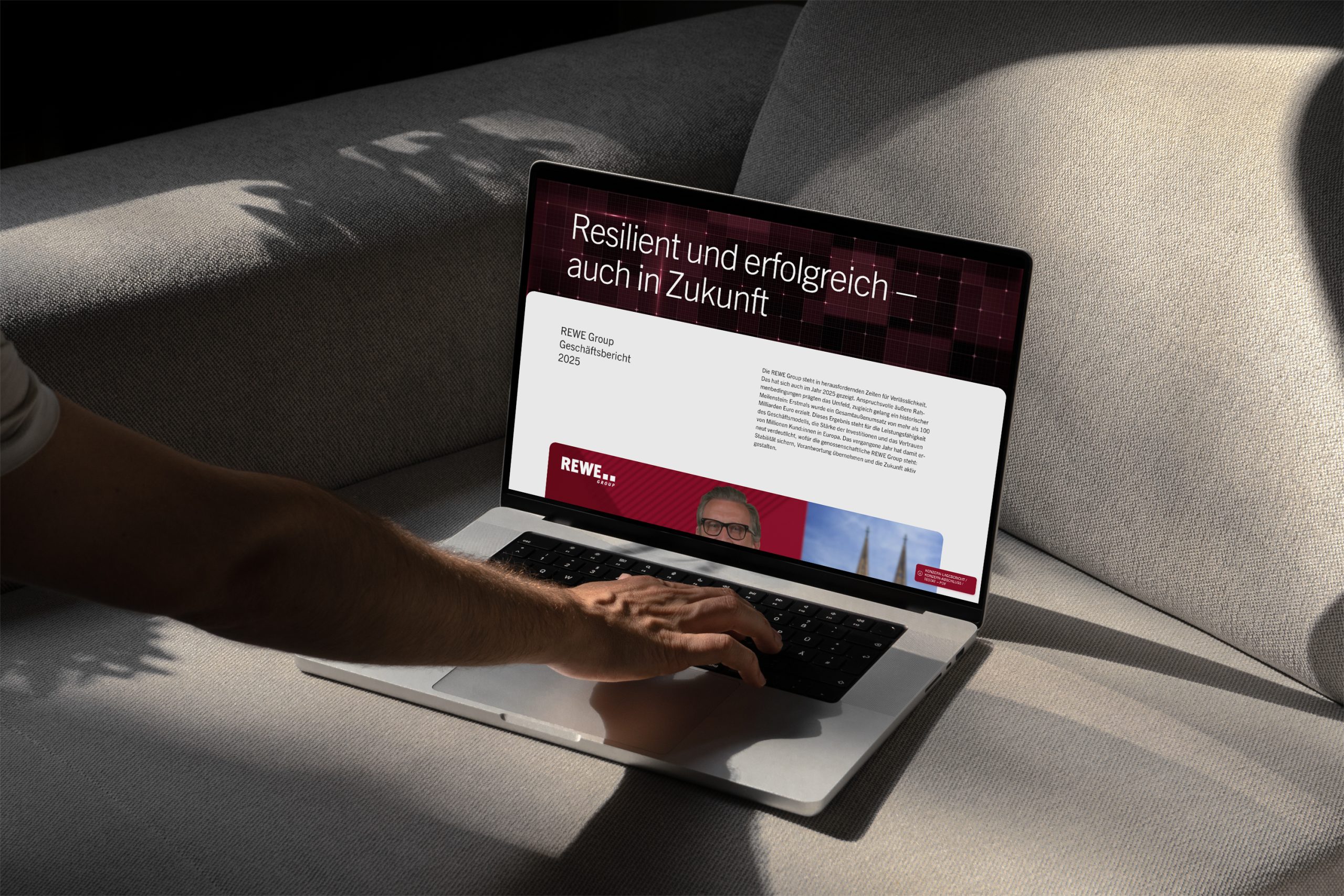 Geöffneter Laptop auf einer Ablage aus Edelstahl. Auf dem Bildschirm ist die Startseite des Geschäftsberichts der REWE Group 2025.