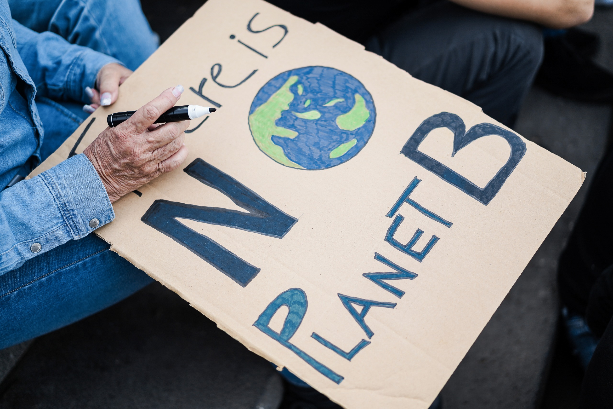 Person hält ein handgemaltes Protestschild aus Pappe mit der Aufschrift 