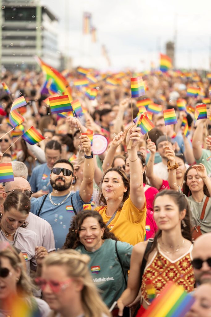 Teilnehmende eines Christopher Street Day mit zahlreichen Regenbogenflaggen in einer dicht gefüllten Menschenmenge.