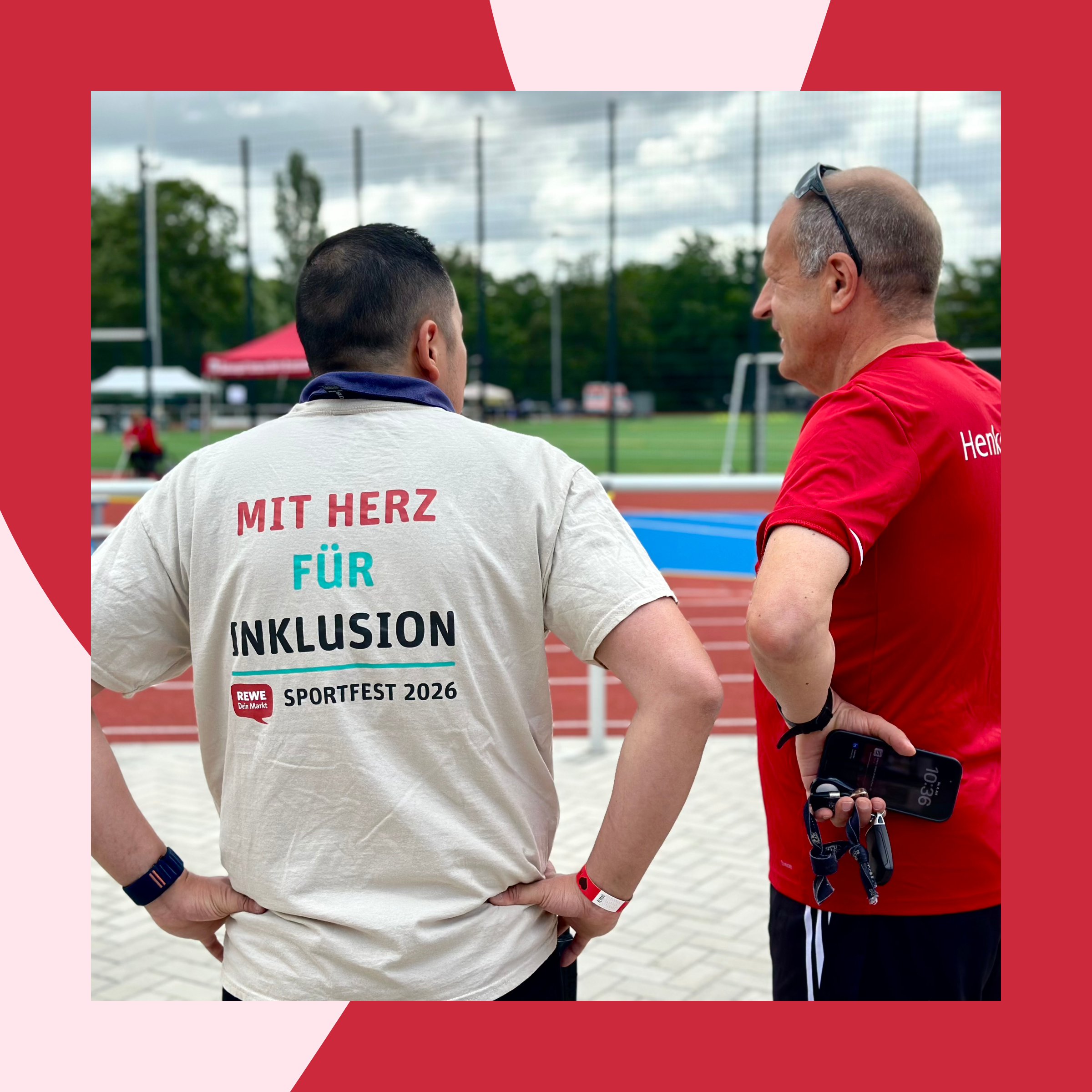 Two people are standing at an athletics and sports complex, looking out at the event grounds. One person’s T-shirt reads “With Heart for Inclusion – Sports Festival 2026.”