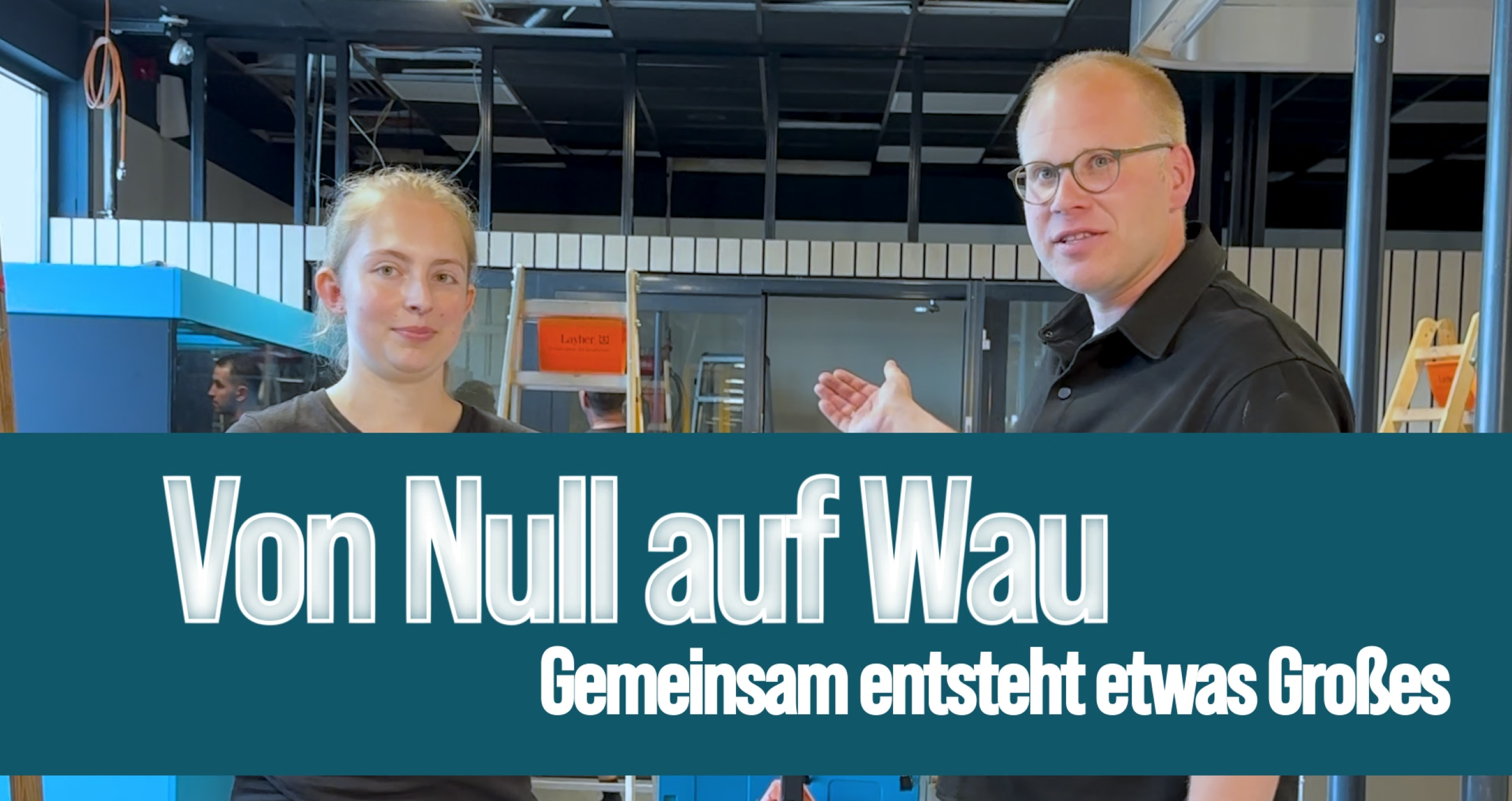 Two people at a construction site with the slogan “From Zero to Wau—Together We’re Building Something Great.”