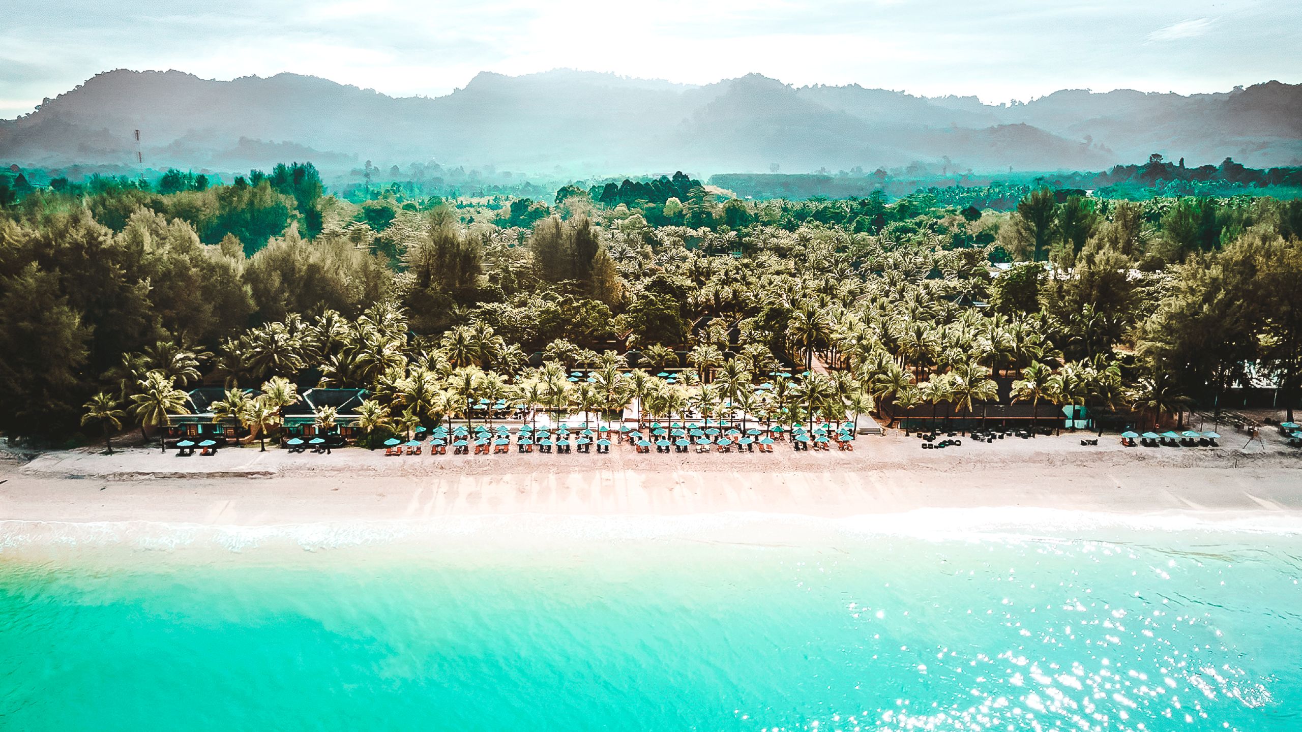 Poollandschaft des Hotels ananea Beyond Khao Lak in Thailand mit Liegen, Sonnenschirmen, Palmen und moderner Resort-Architektur.