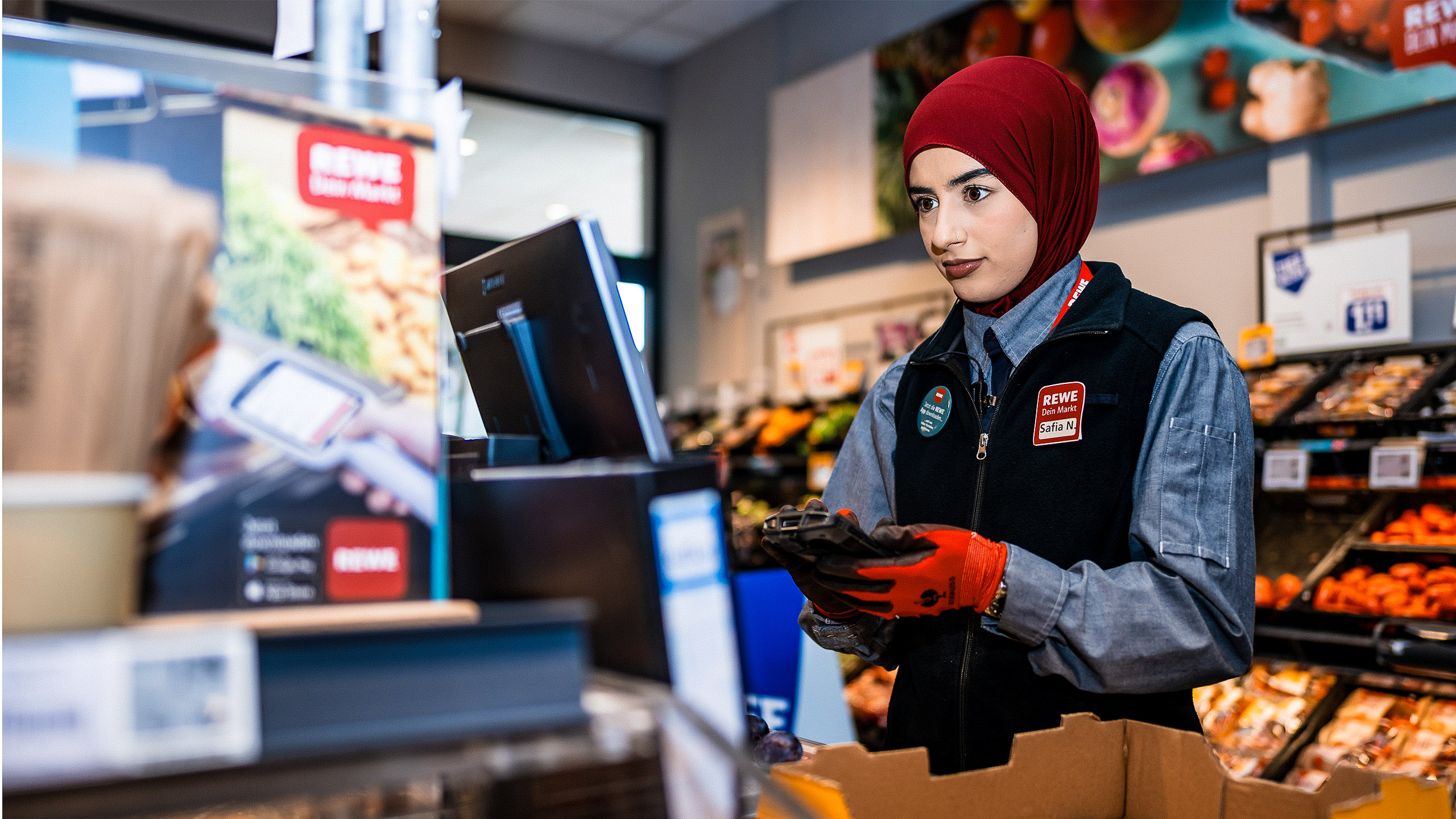 Person in REWE-Arbeitskleidung an einer Kasse in einem REWE Markt.