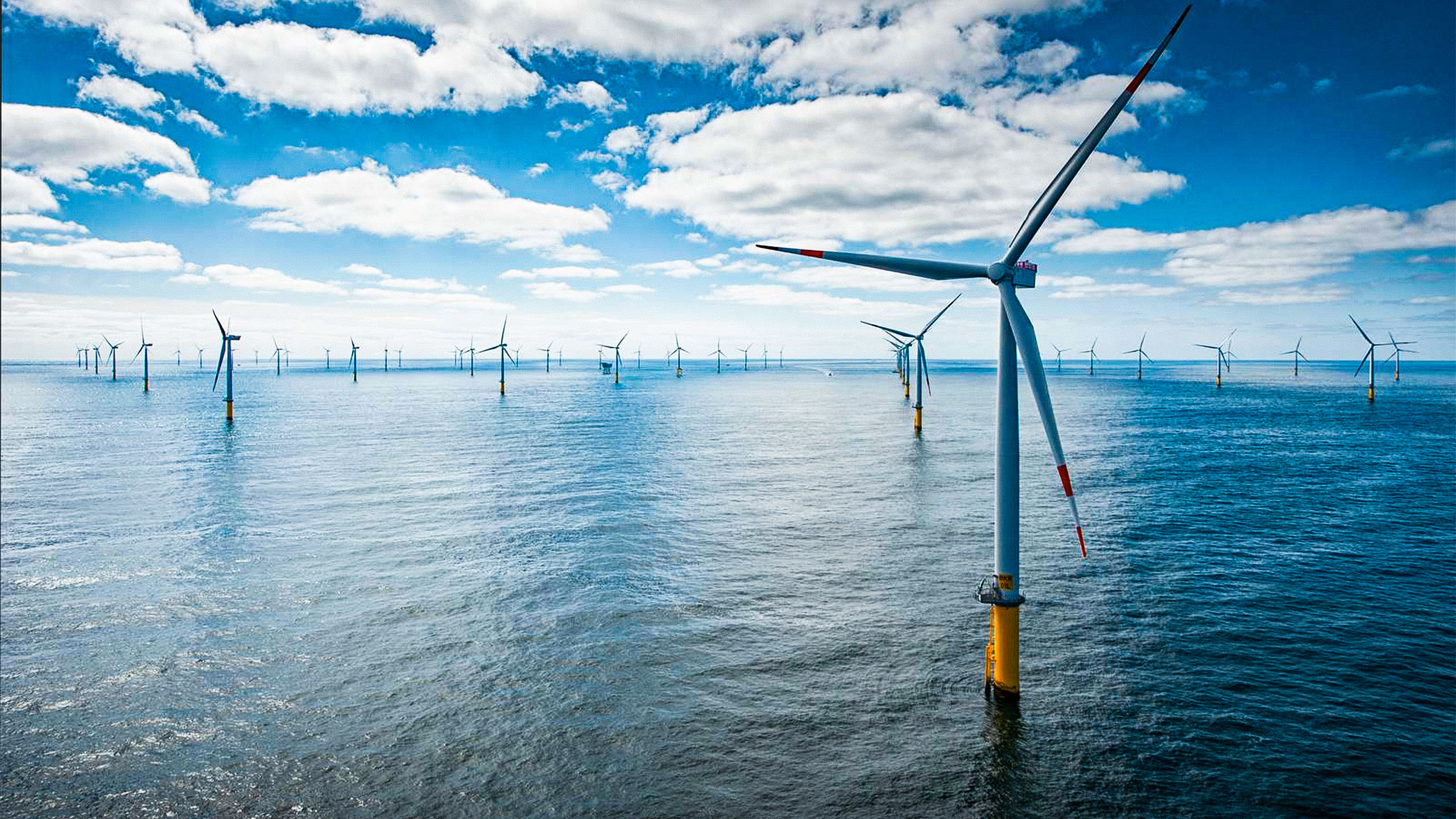 Offshore-Windpark mit zahlreichen Windkraftanlagen im Meer unter blauem, teils bewölktem Himmel.