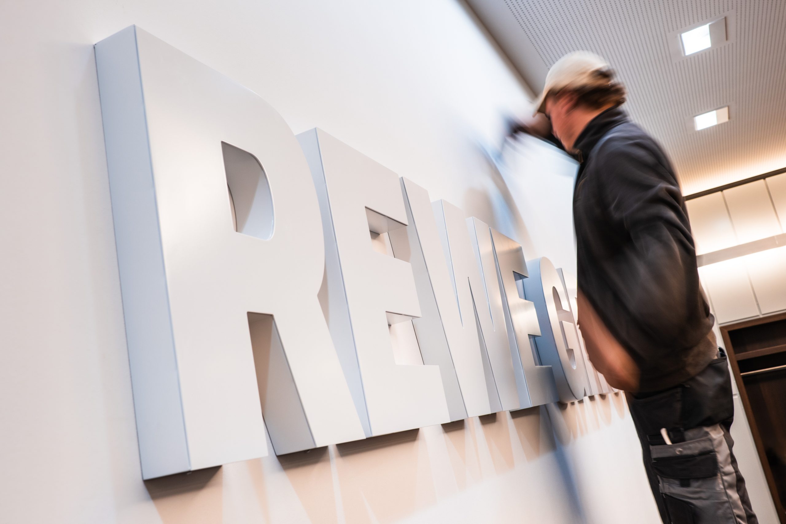 Person arbeitet an einer hellen Wand mit großen, weißen 3D-Buchstaben, die 
